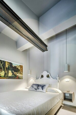 Ein modernes Schlafzimmer mit einem großen Bett, einem Bild an der Wand und einem kleinen Nachttisch.