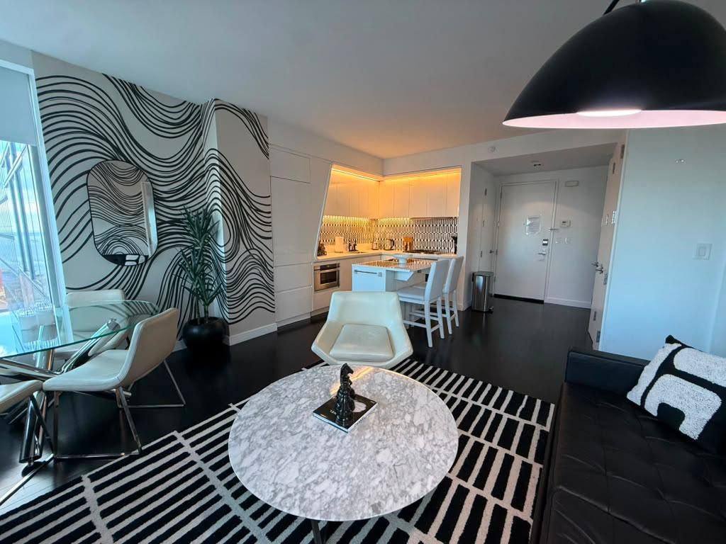 Un salon moderne avec une table à manger en verre, des chaises blanches, une table basse ronde et un luminaire suspendu noir.