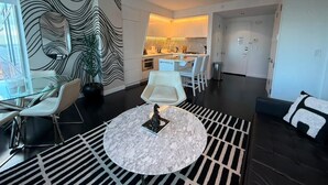 En moderne stue med et glasbord, hvide stole, et rundt sofabord og en sort hængende lampe.