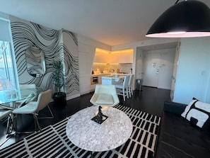 Ein modernes Wohnzimmer mit einem Glastisch, weißen Stühlen, einem runden Couchtisch und einer schwarzen Pendelleuchte.