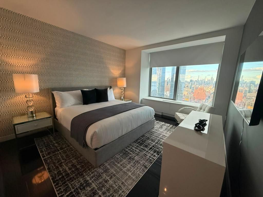 A modern hotel room with a large bed, a desk, and a city view.