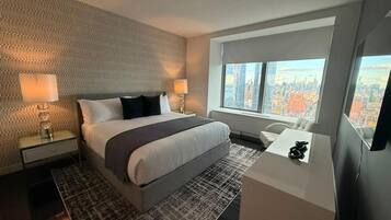 A modern hotel room with a large bed, a desk, and a city view.