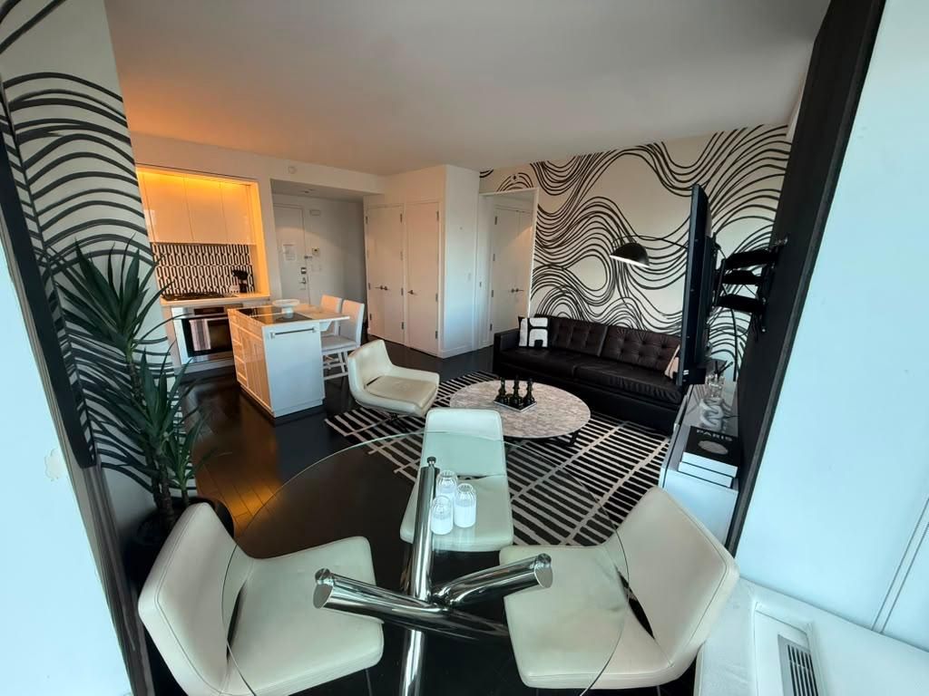 A modern living room with a dining area, a sofa, and a kitchen in the background.