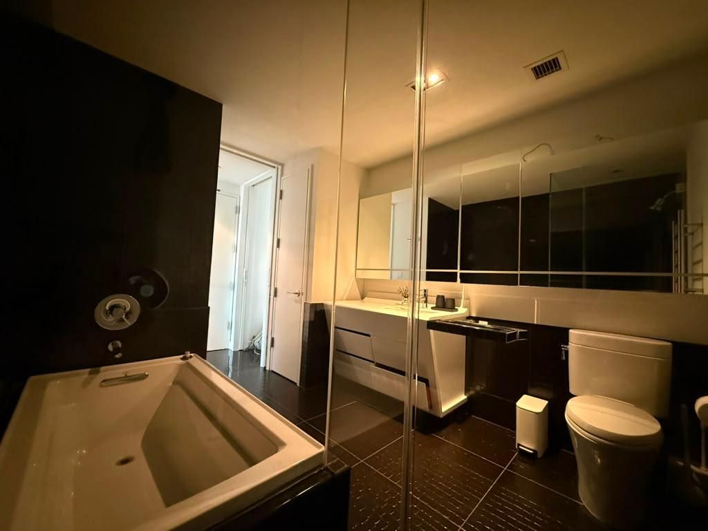 Une salle de bain moderne avec un grand miroir, une baignoire, des toilettes et un lavabo.