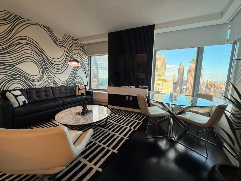 A modern living room with a black sofa, a glass coffee table, and a dining area with a glass table and chairs.