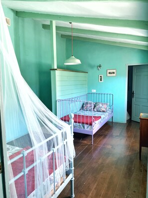 A room with a bed, a cot with a canopy, a hanging light fixture, and a door.