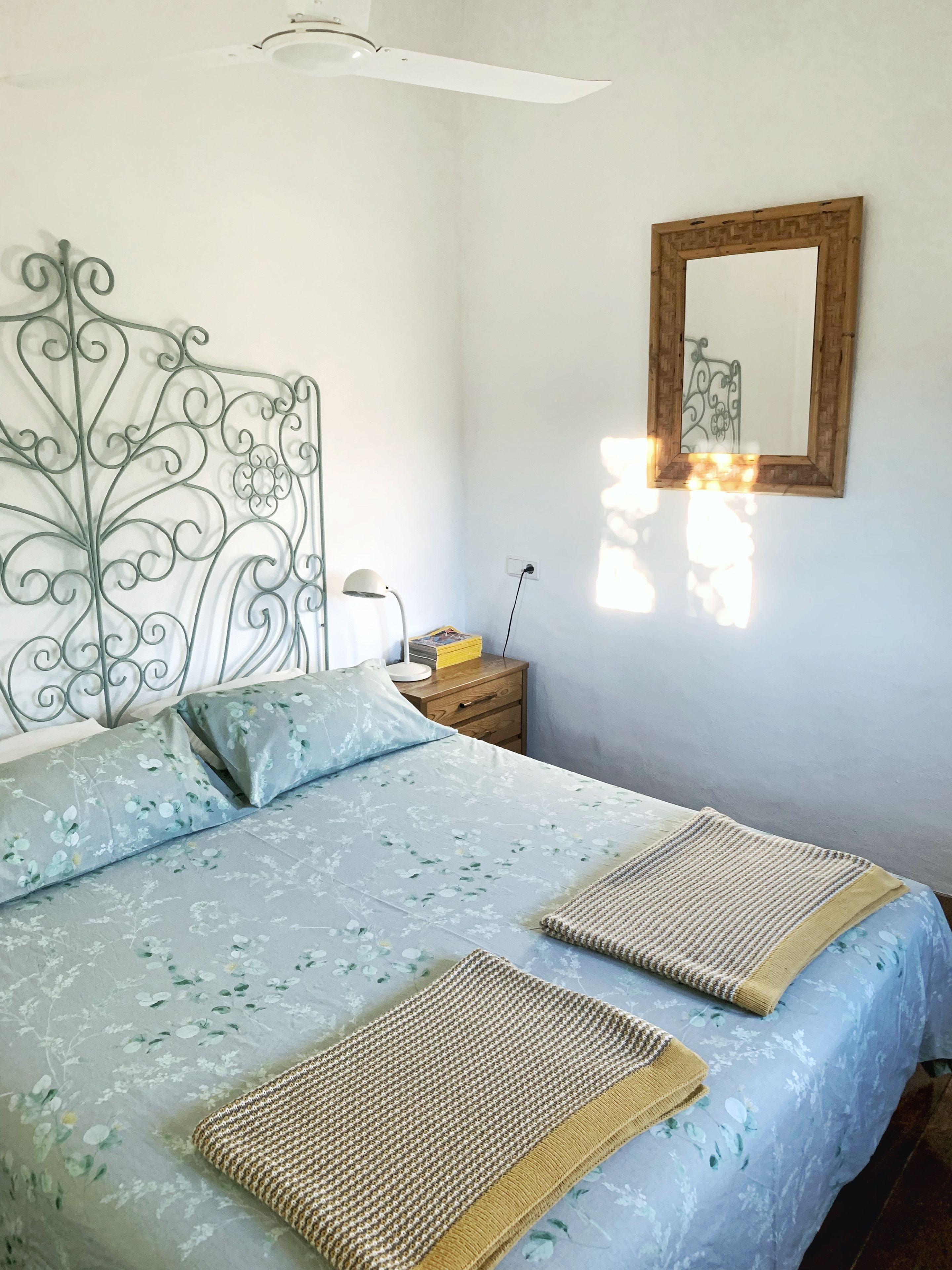 A bedroom with a bed, a nightstand, a lamp, and a mirror.
