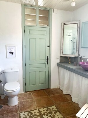 A bathroom with a toilet, a green door, a shower, and a sink with a mirror.