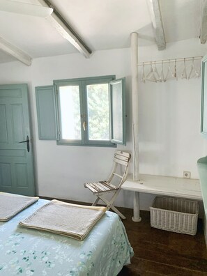 A room with a bed, a chair, a window, a door, and a wall-mounted shelf. - Charming Rural Lodging in the Sierra de las Nieves · Casa Algarrobo (Tolox)