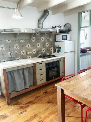 A compact kitchen with a gas stove, oven, microwave, and a sink. There is a wooden table and red chairs in the dining area.