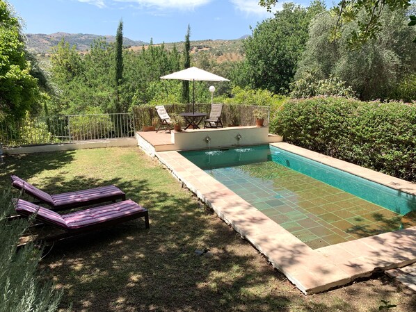 A backyard with a swimming pool, lounge chairs, and a patio table with an umbrella.