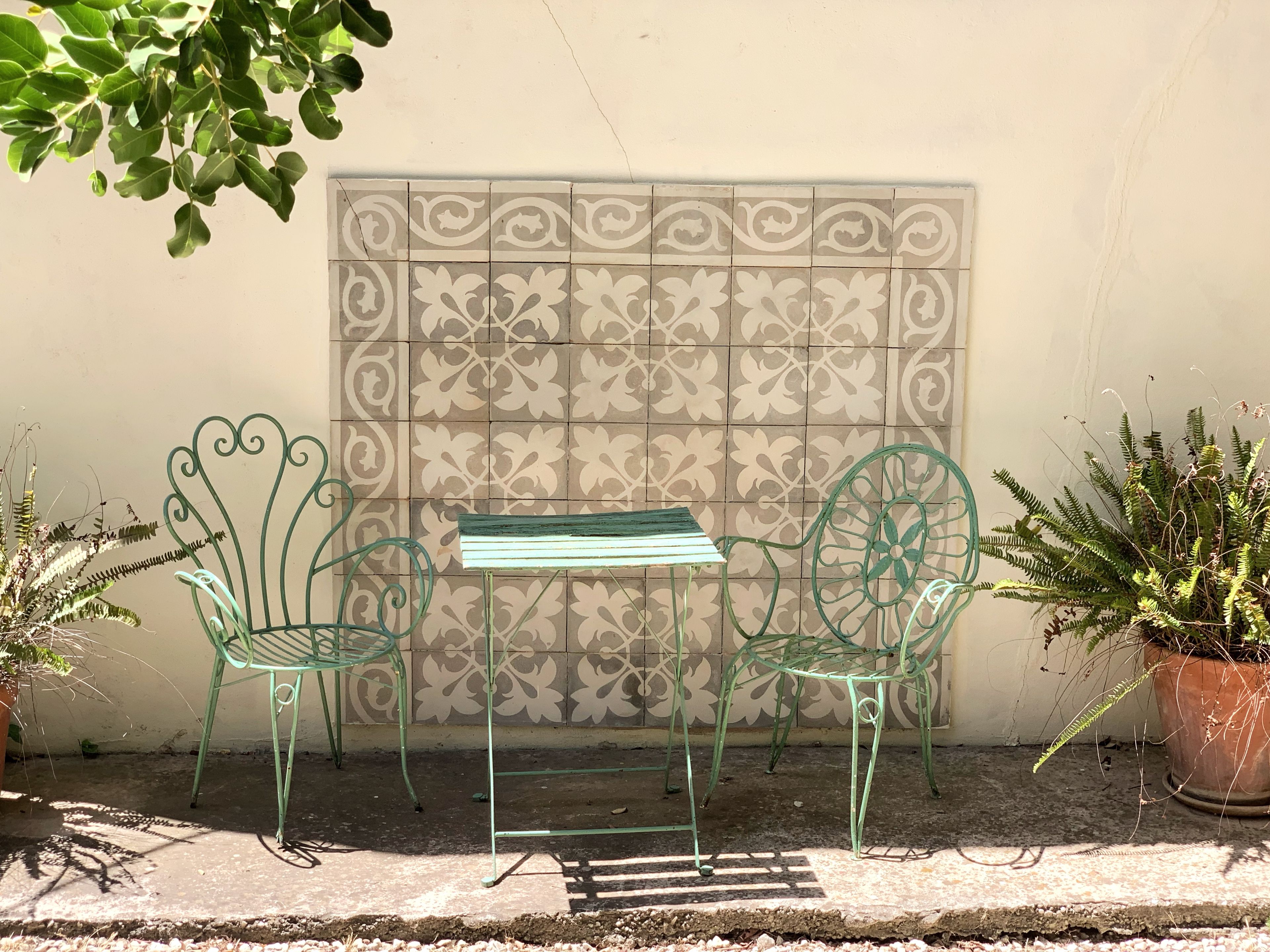 A small outdoor seating area with a metal table and chairs, a decorative wall, and potted plants.