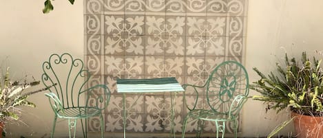 A small outdoor seating area with a metal table and chairs, a decorative wall, and potted plants.