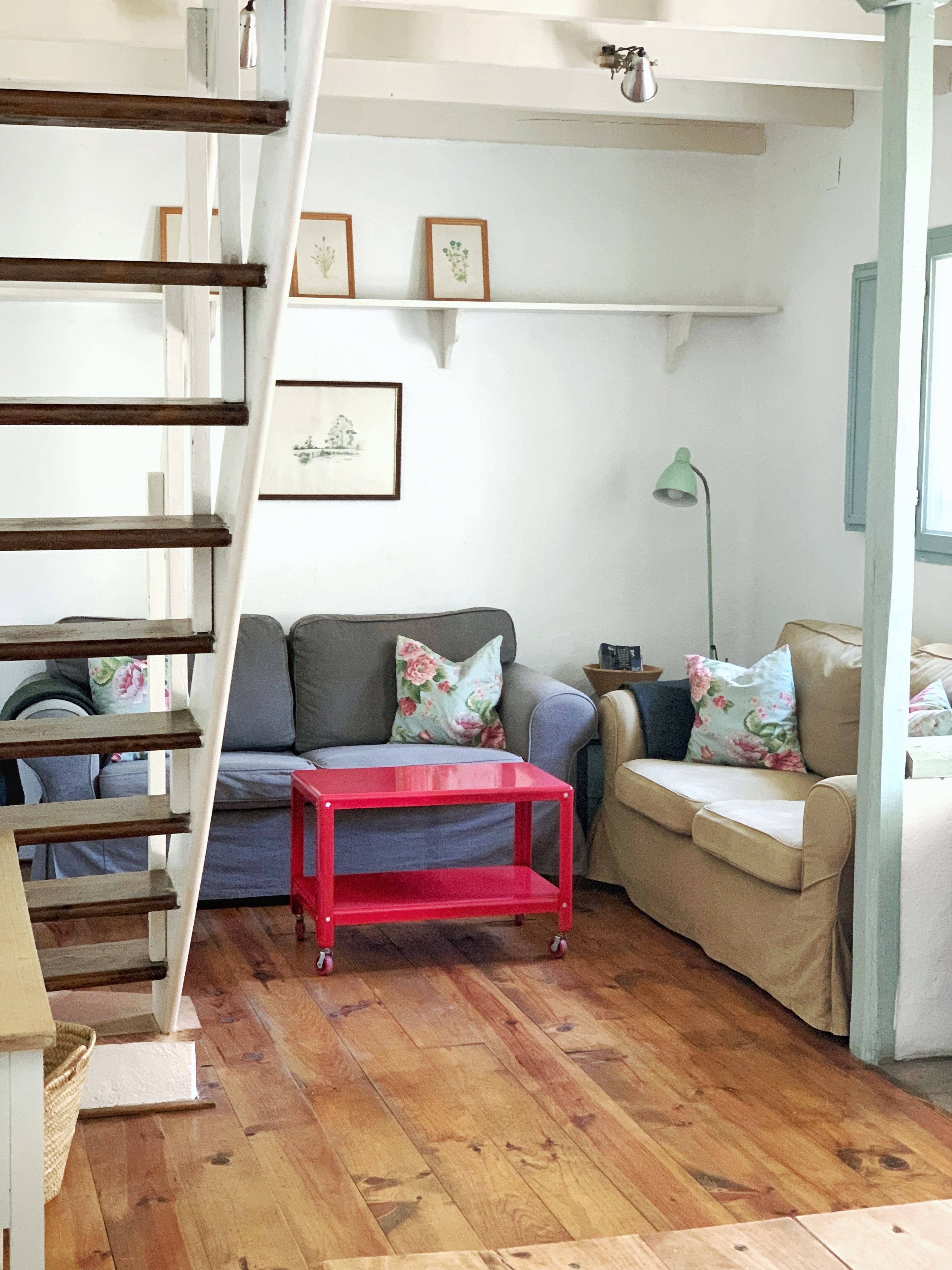 A living room with a staircase, a red table, a grey sofa, and a beige sofa.