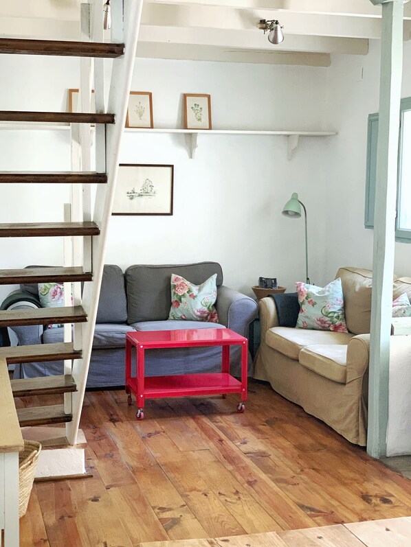 A living room with a staircase, a red table, a grey sofa, and a beige sofa.