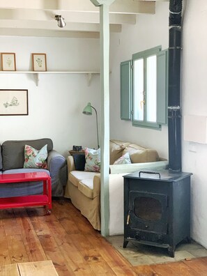 A cozy living room with a sofa, a red table, a green lamp, and a black wood-burning stove. - Charming Rural Lodging in the Sierra de las Nieves · Casa Algarrobo (Tolox)