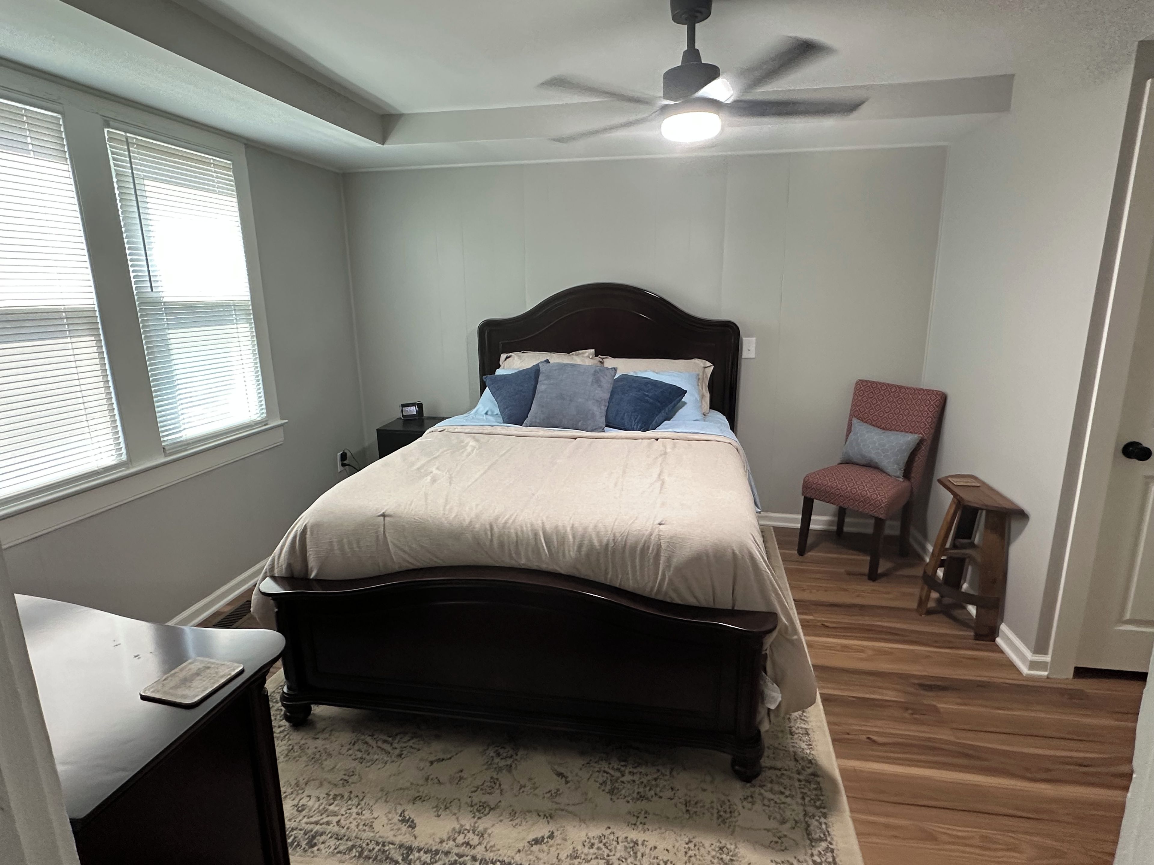 A bedroom with a bed, a chair, a nightstand, and a ceiling fan.