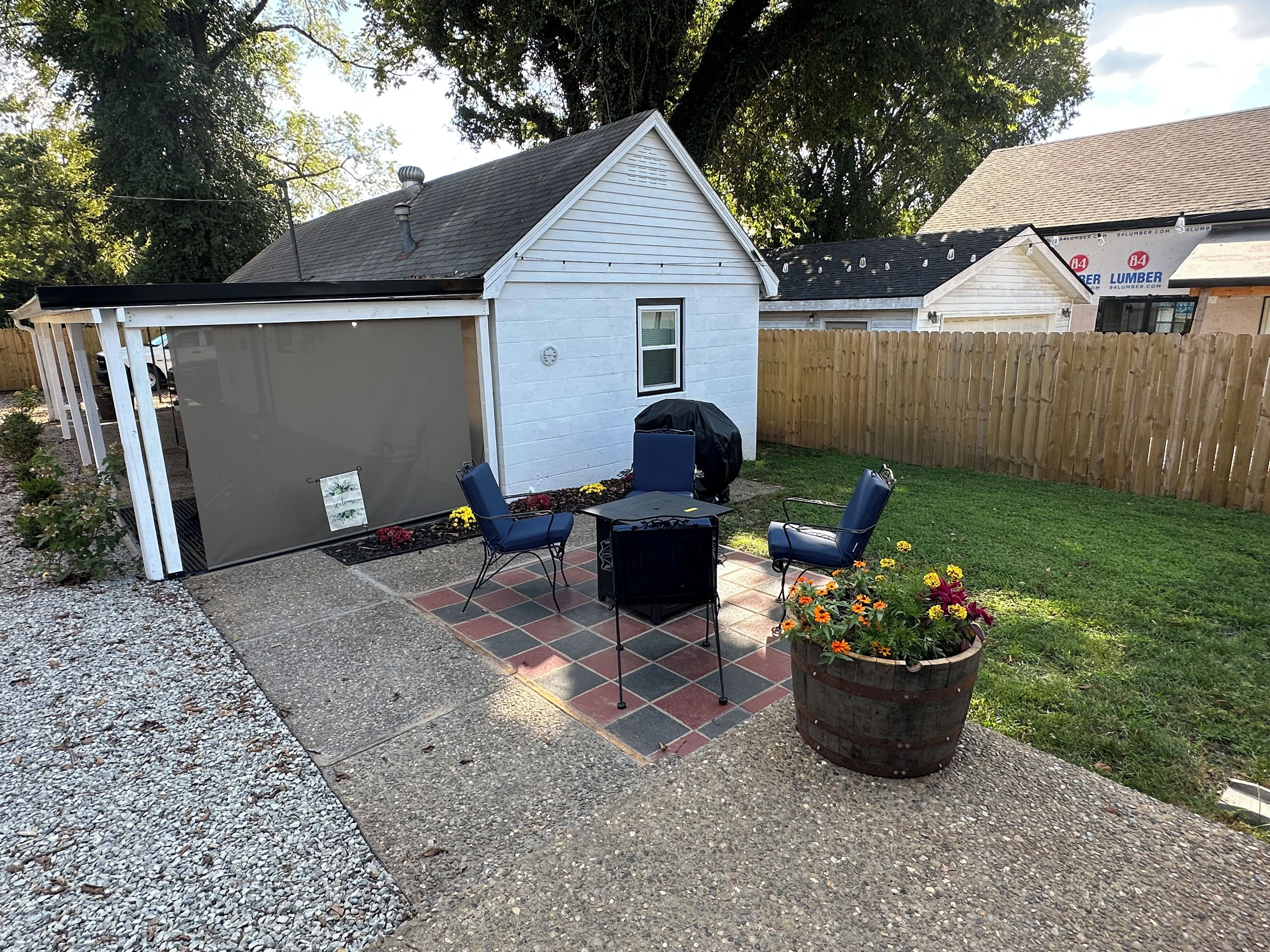 A backyard patio with a grill, two chairs, and a potted plant.
