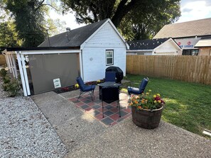 A backyard patio with a grill, two chairs, and a potted plant.