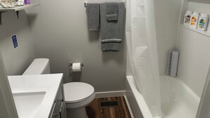 A compact bathroom with a toilet, sink, shower, and a small shelf with toiletries. - Welcome to “The Hideaway”..a cozy chalet in the heart of the Bourbon Capital (Bardstown)