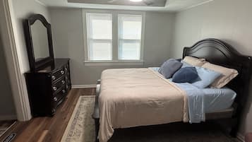 Une chambre à coucher comprenant un lit, une commode, un miroir, un ventilateur de plafond et une fenêtre avec des stores.