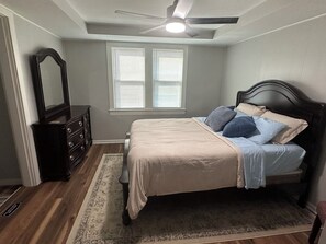 A bedroom with a bed, dresser, mirror, ceiling fan, and window with blinds.