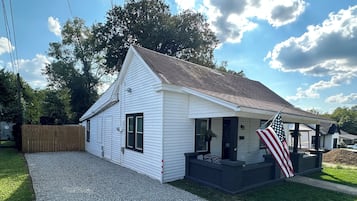 A single-story house with a gravel driveway, a wooden fence, and an American flag.