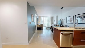 A modern kitchen with a dishwasher, a dining area with a table and chairs, and a view of the city through large windows. - ICON Brickell High-Floor Condo, City Views, Pool & Spa (Miami)