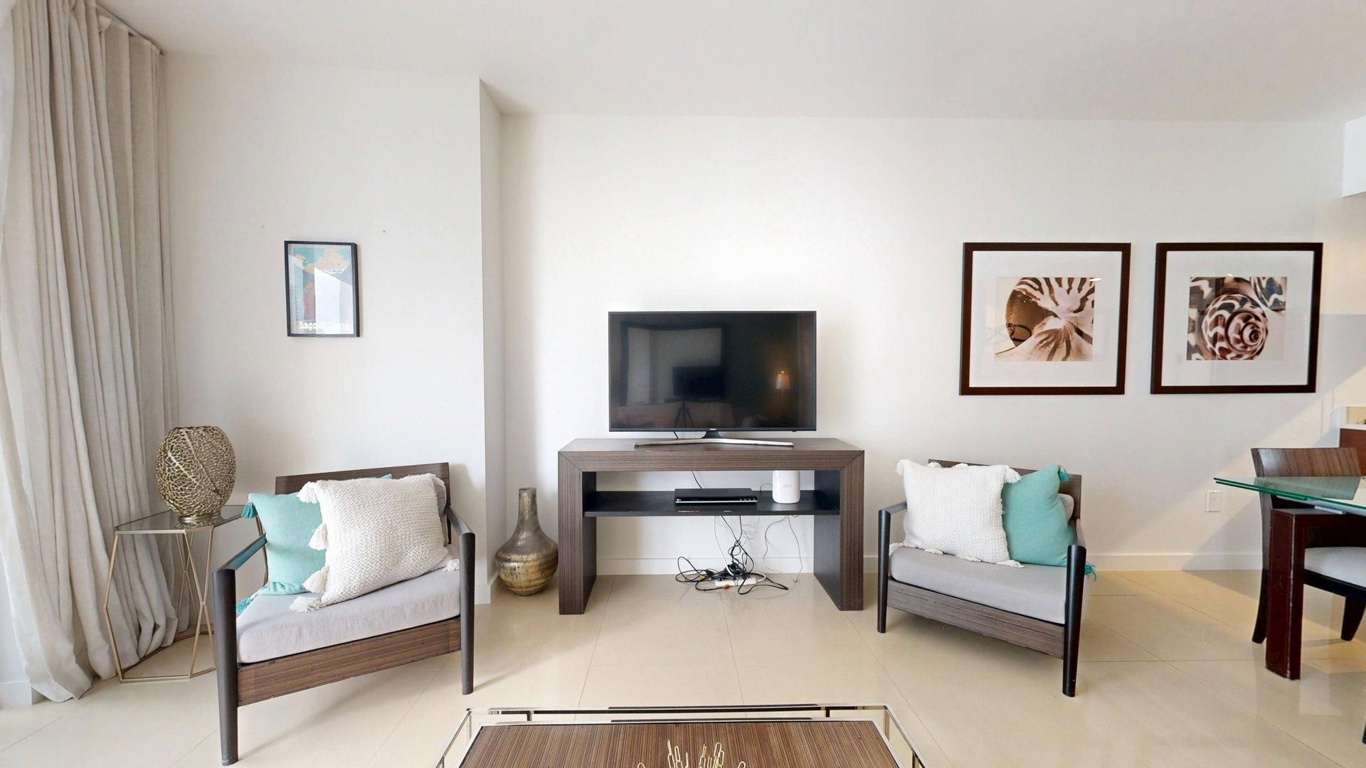 A modern living room with a flat-screen TV, two sofas, a coffee table, and artwork on the walls.
