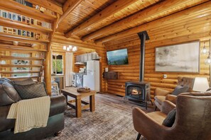 Interior acogedor de una cabaña de troncos con chimenea, muebles de madera y un ventanal grande.