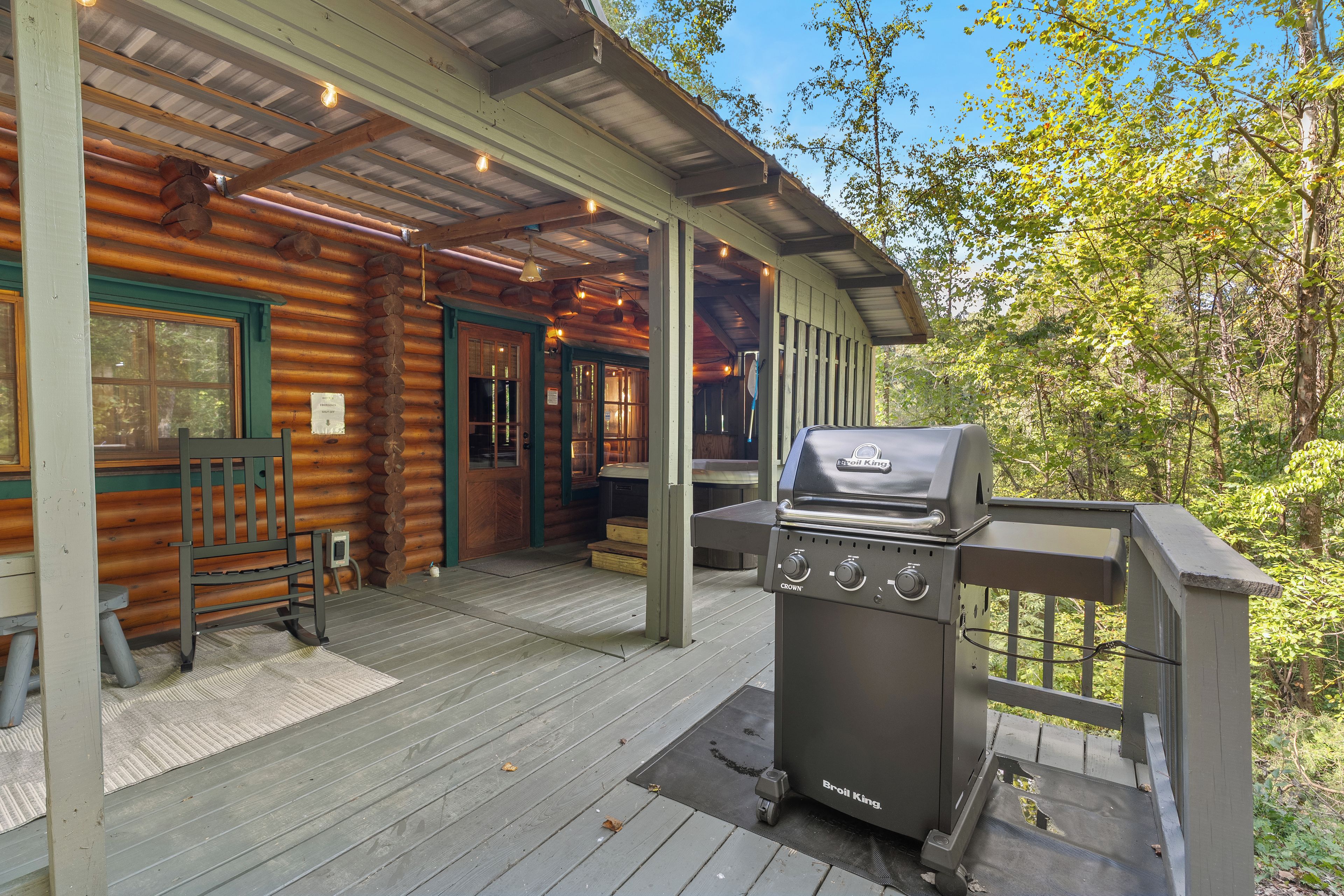 A wooden cabin with a covered porch, a grill, and a bench.
