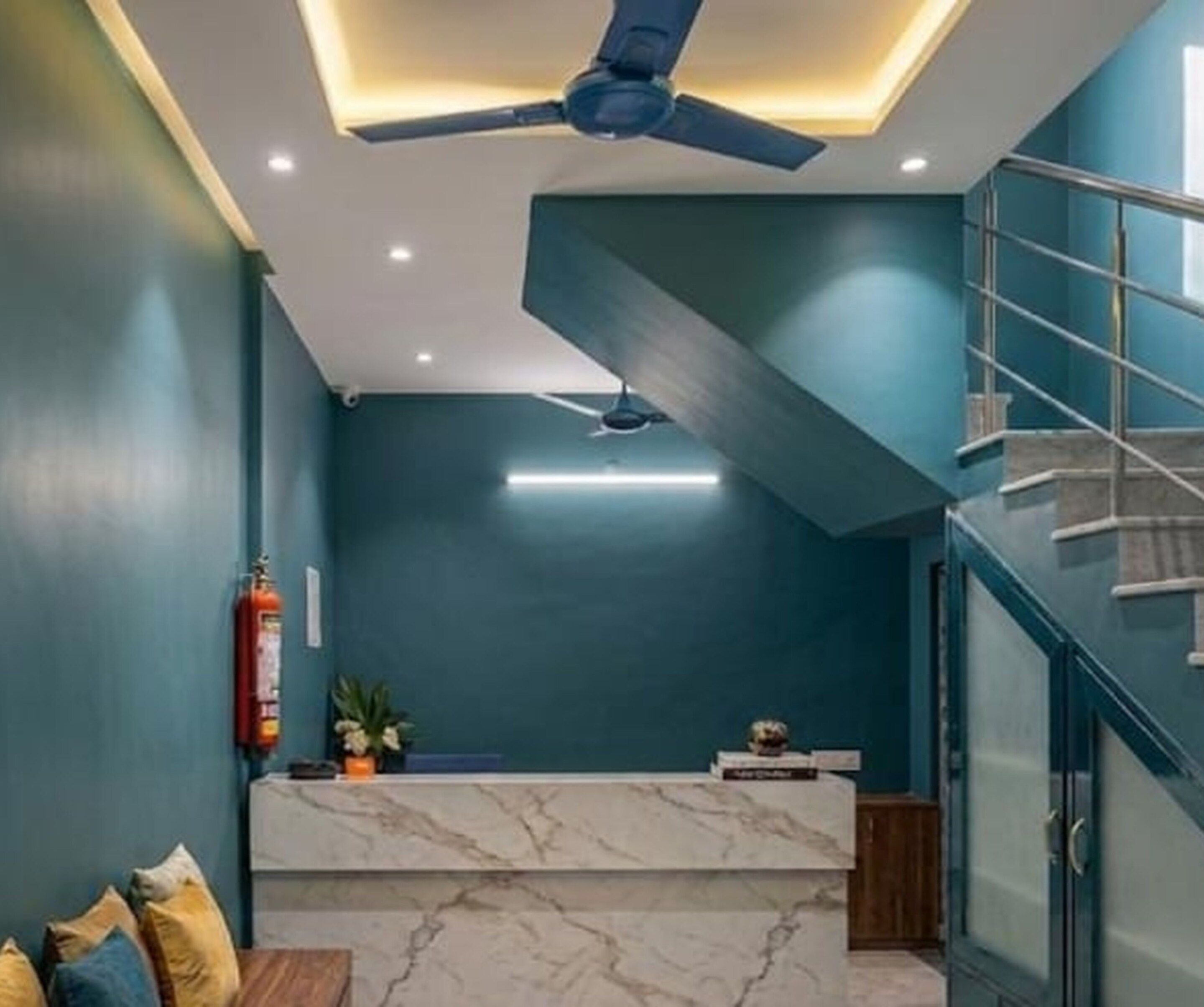 A modern interior with a marble reception desk, ceiling fans, and a staircase.