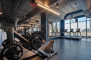 A gym with weightlifting equipment, treadmills, and large windows offering a city view. - Deluxe E11EVEN Studio Suite with Elite Amenities (Miami)