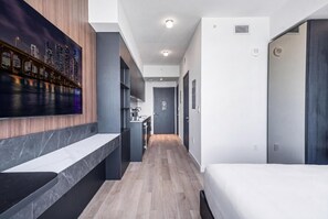 A modern hotel room with a long hallway, a bed, a desk, and a cityscape view. - Deluxe E11EVEN Studio Suite with Elite Amenities (Miami)