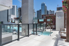 Une piscine sur le toit, entourée de rampes de verre, offrant une vue sur les gratte-ciel de la ville, et une horloge fixée au mur.