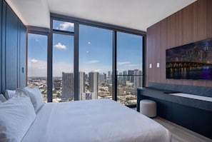 A modern hotel room with a large bed, a seating area, and a city view through expansive windows. - Deluxe E11EVEN Studio Suite with Elite Amenities (Miami)