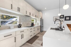 Una cucina moderna con mobili chiari in legno, un frigorifero in acciaio inossidabile e un piano di lavoro bianco.