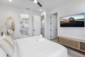 Ein modernes Hotelzimmer mit Bett, Fernseher, Spiegel und einem Badezimmer mit einer Marmordusche.