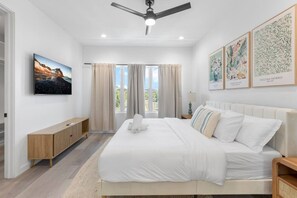 Una camera da letto moderna con un ampio letto, una ventola a soffitto, una TV e opere d'arte alle pareti.