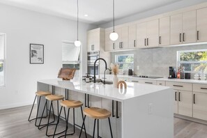 Eine moderne Küche mit Kochinsel, Barhocker und einer Pendelleuchte.