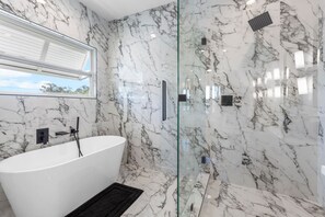Ein modernes Badezimmer mit freistehender Badewanne, einer Duschkabine aus Glas und Marmorwänden.