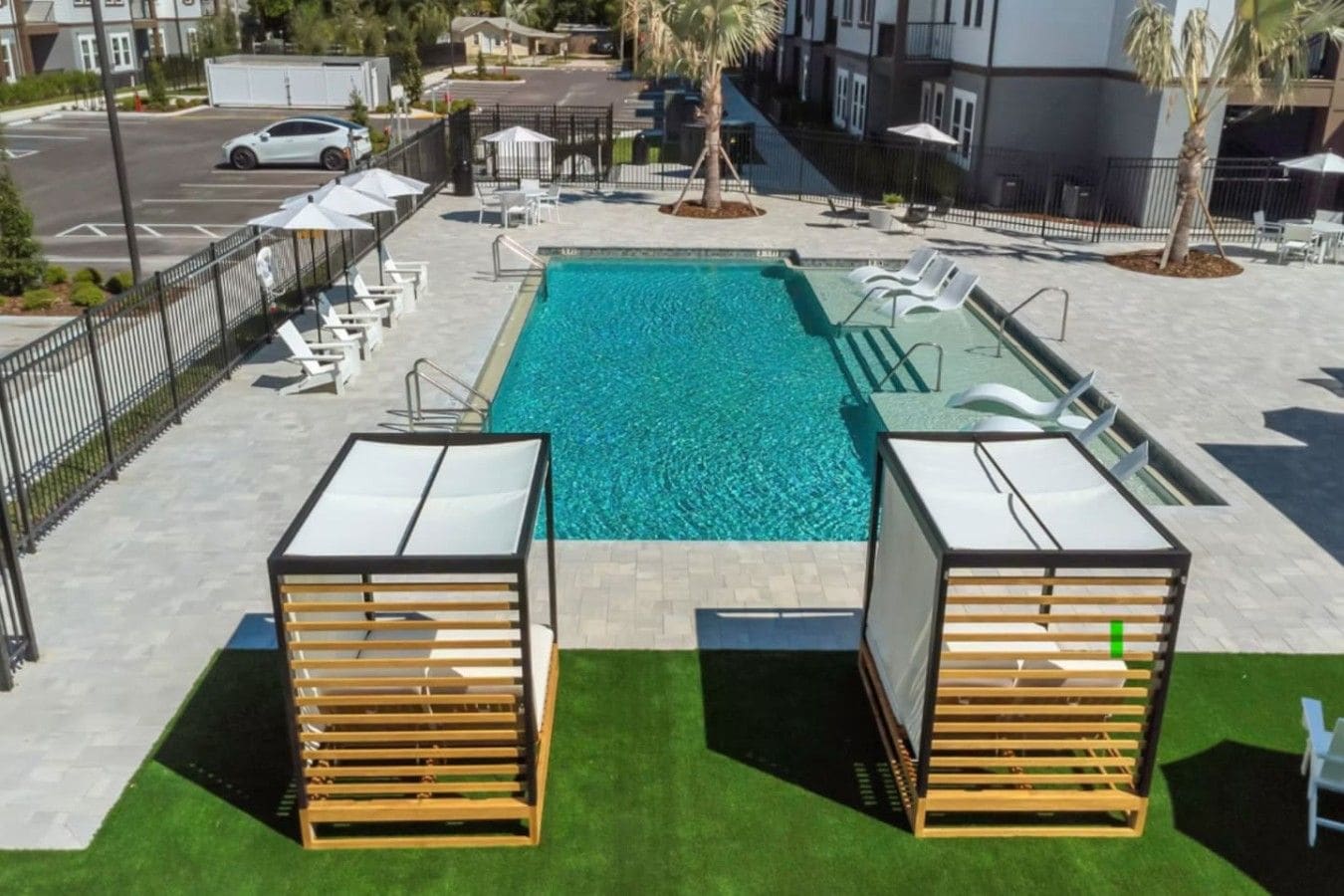 Ein Pool mit Liegestühlen und Sonnenschirmen, umgeben von einem eingezäunten Bereich mit einem gepflasterten Weg.