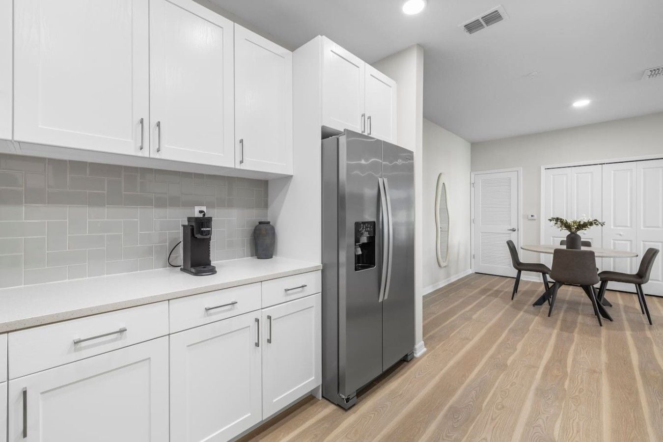 A modern kitchen with white cabinets, a stainless steel refrigerator, and a coffee maker on the counter.