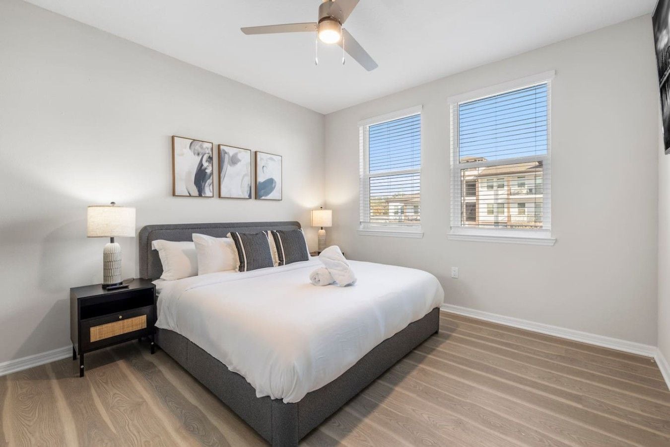 A bedroom with a bed, nightstands, a ceiling fan, and two windows with blinds.