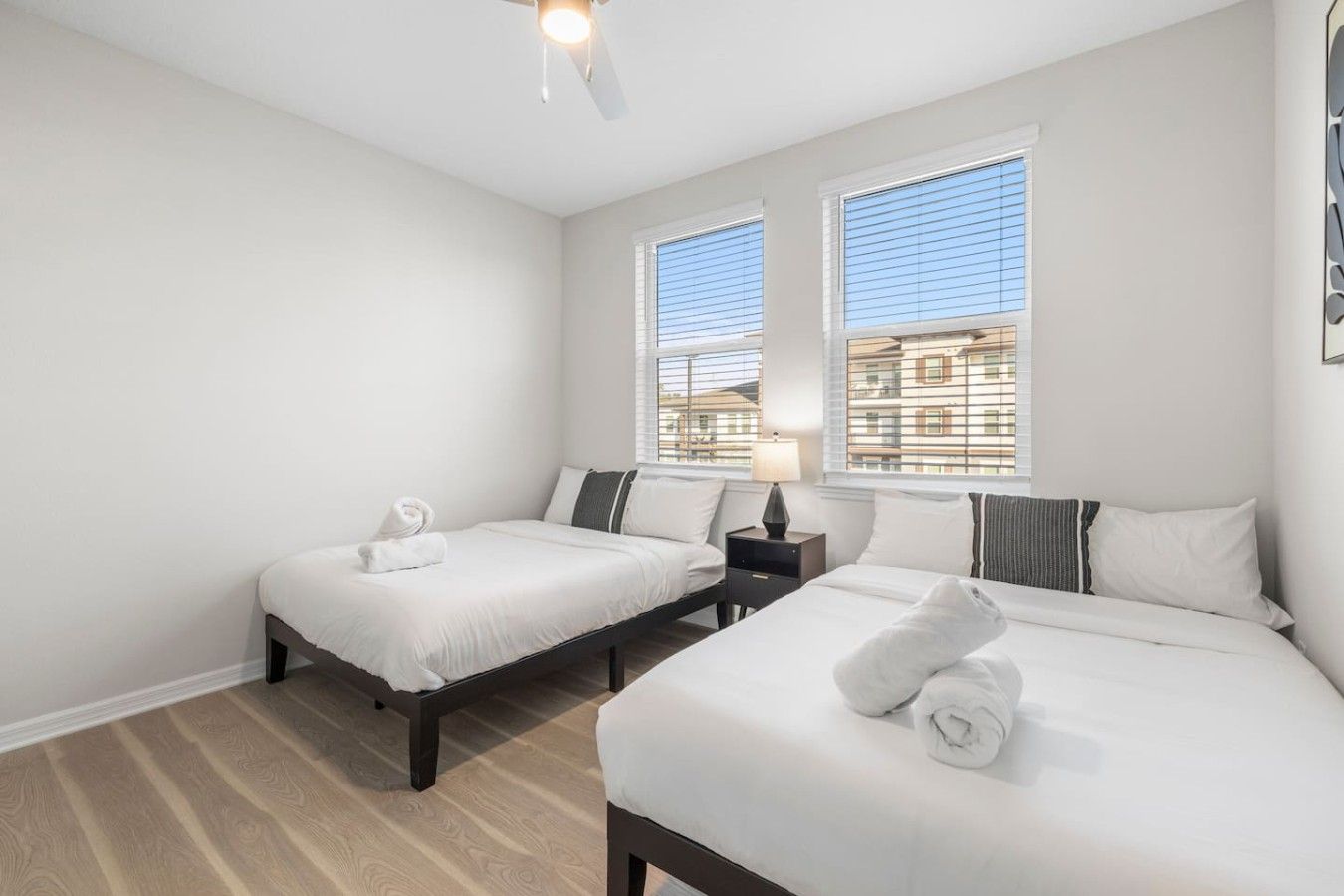 A hotel room with two beds, a ceiling fan, and a window with blinds.