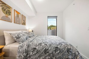 A bedroom with a bed, a nightstand, a window, and wall art. - 2 Bed | Cgy Tower View | AC | Underground Parking (Calgary)
