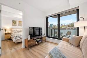 A modern bedroom with a large window, a bed, a TV, and a balcony with city views. - 2 Bed | Cgy Tower View | AC | Underground Parking (Calgary)