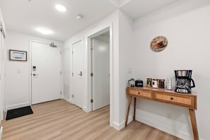 A hallway with white doors, a coffee station with a coffee maker, and a wall clock. - 2 Bed | Cgy Tower View | AC | Underground Parking (Calgary)