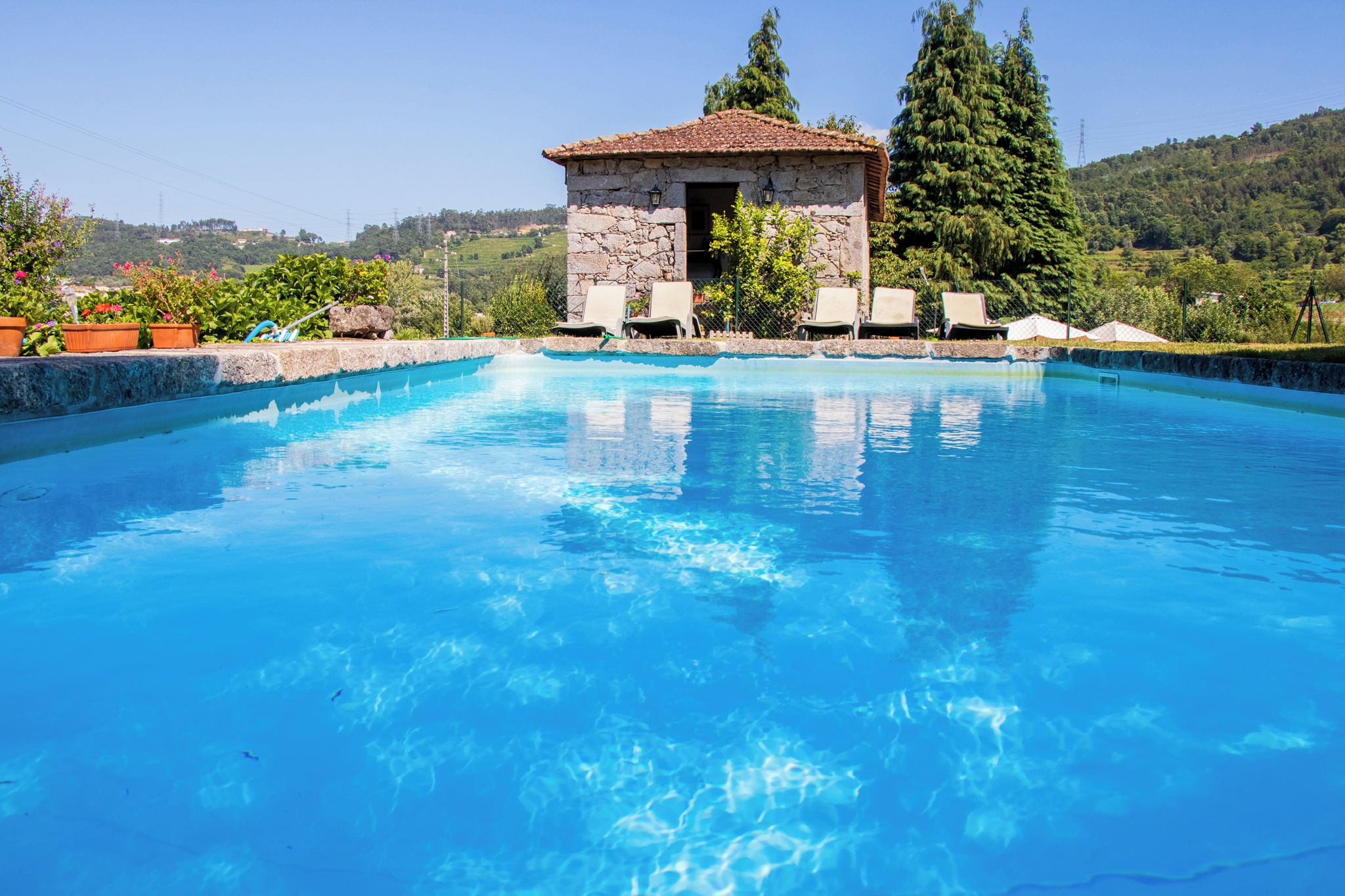 Une piscine avec un bâtiment en pierre et des chaises longues à l’arrière-plan.