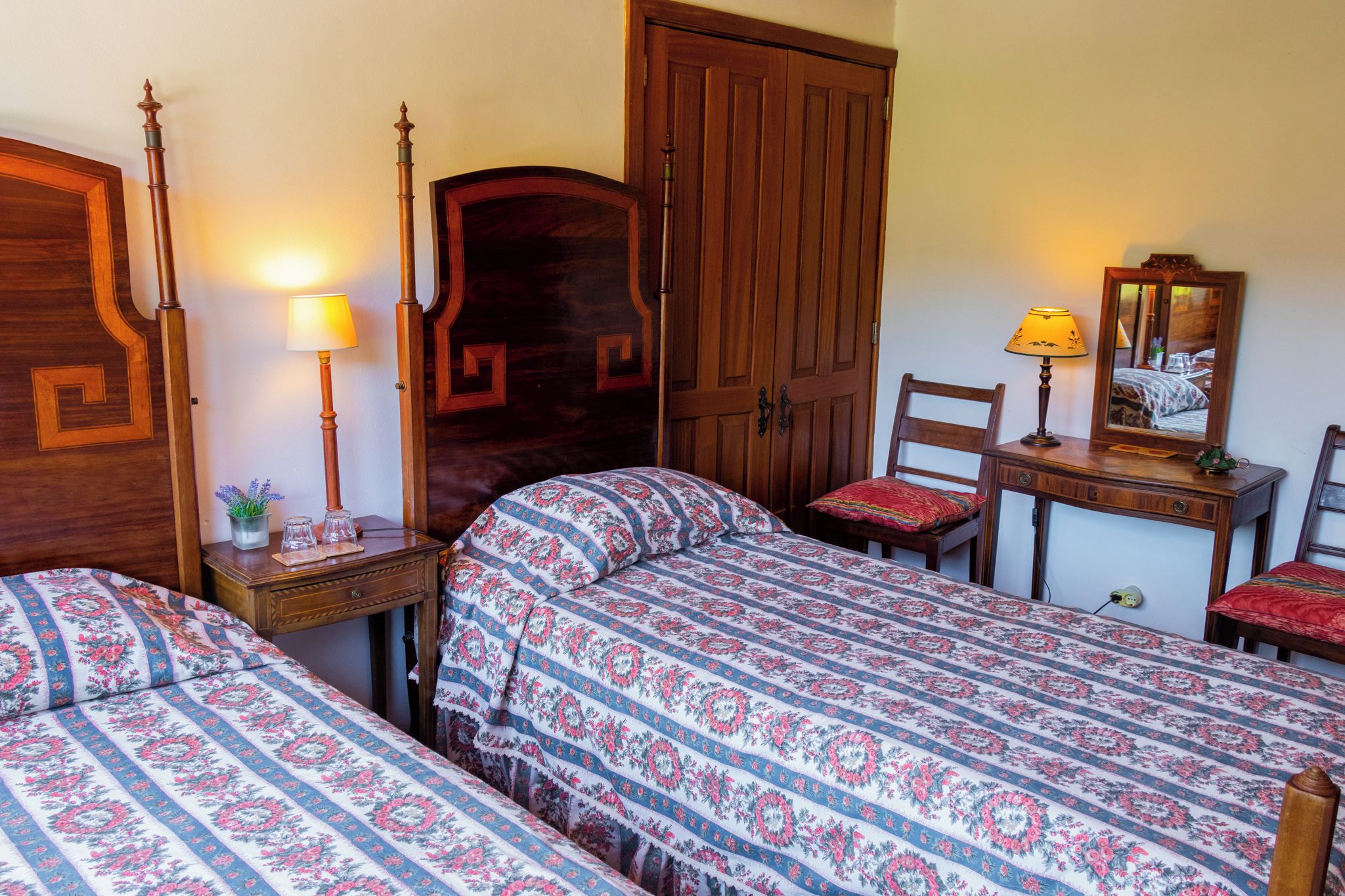 Un dormitorio con dos camas individuales, un armario de madera, un escritorio con silla y una mesita de noche con lámpara.